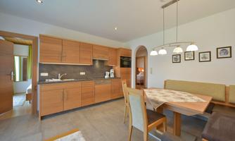 A modern kitchen with wooden cabinets and a dining area. The room is bright and friendly with neutral color tones.