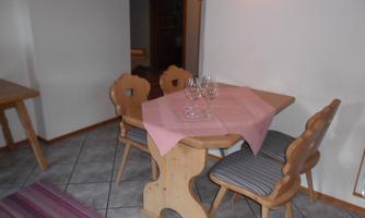 A small dining area with a wooden chair design and a table decorated with a pink tablecloth. There are glasses on the table and the floor is tiled.