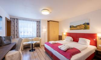 A modern hotel room with a large bed, a table, and chairs. The room is bright and cheerfully decorated, with a window and a beautiful wall mural.