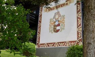 A charming building with an artistic mural and a coat of arms. The green lawn and the surrounding trees give the scene an inviting atmosphere.