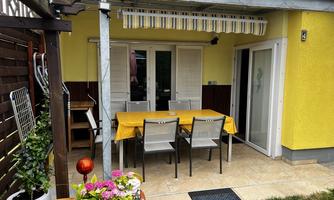 An inviting outdoor area with a large table and chairs on a terrace. The walls are painted yellow, and colorful plants decorate the space.