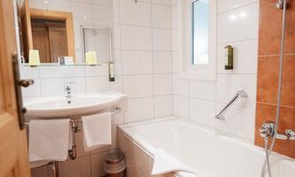 A modern bathroom with a bathtub and a sink. The walls are light tiled and there is a large mirror.
