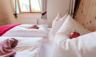 A cozy bedroom with two beds and white pillows. On the bed lies a red apple and a checked cloth.