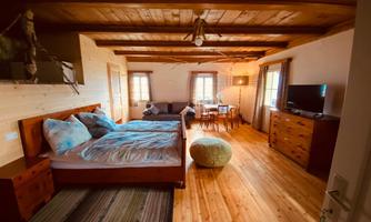 A cozy room with wooden ceilings and a double bed. The room has a living area with a sofa, table, and television.