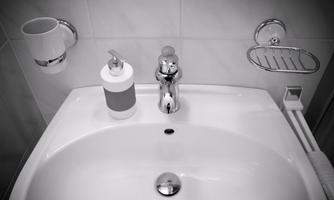 A modern sink with a shiny faucet. Next to the sink are soap dispensers and a cup.