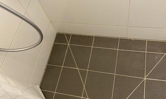 A modern bathroom with a shower area. The floor is tiled with gray tiles, and there is a channel for water drainage.