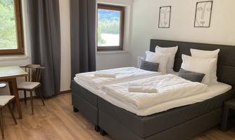 A cozy bedroom with a double bed and two chairs. The large windows let in plenty of light and offer a view of the greenery.