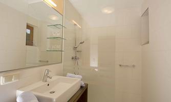 A modern bathroom with a shower and an elegant sink. Bright tiles and a large mirror wall create an airy impression.