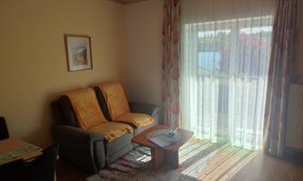 A cozy living room with a sofa and a table. Large windows let in plenty of daylight.