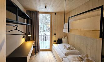 A modern room with wood paneling and large windows. There are two single beds and a desk with a lamp.
