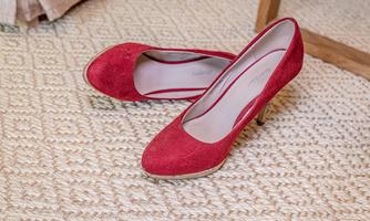 Red high-heeled shoes made of suede are lying on a light carpet. The shoes have an elegant shape and go well with various outfits.