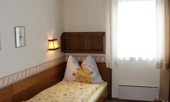 A simple room with two single beds and natural wood details. The window lets in plenty of daylight and the walls are painted in light colors.