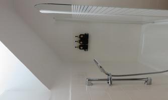 A modern shower with clean lines and a bright, neutral design. Three bottles for shower products are mounted on the wall.