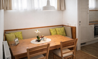 A cozy dining area with a wooden table and chairs. On the table, there is an orchid and some decorative elements.