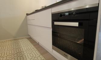 A modern kitchen with white cabinets and a built-in oven. The floor is decorated with a light carpet pattern.