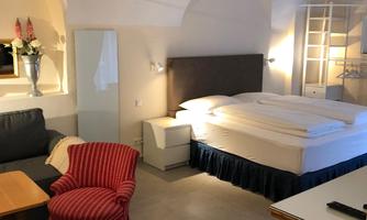 A cozy room with a double bed and a red armchair. There is a table and modern furnishings.