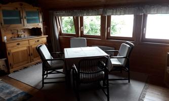 A cozy dining area with a round table and four chairs. Large windows provide plenty of daylight and a view of the greenery.