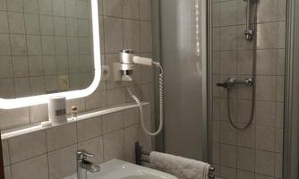 A modern bathroom with a shower cabin and a sink. The walls are brightly tiled, and there is a lit mirror.