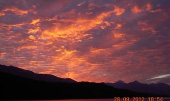 A spectacular sunset with colorful clouds over a calm lake. Gentle mountains are visible in the background.