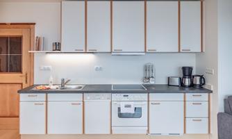 A modern kitchen with white cabinets and a gray countertop. It includes various appliances such as a coffee maker and a dishwasher.