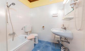 A modern bathroom with a bathtub, toilet, and sink. The walls are tiled and the floor is blue.
