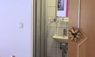A bathroom with a shower, a sink, and a mirror. The floor is covered with a red carpet and the walls are tiled.