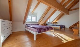 A bright room with two beds and wooden supports. There is a window that lets in a lot of daylight.