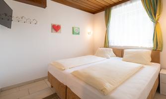 A cozy bedroom with two beds and bright curtains. There are artworks on the wall and plenty of natural light.