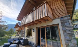 A modern wooden house with a balcony and a porch. The cozy outdoor seating area invites you to relax.