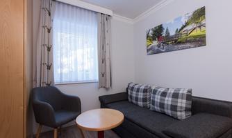 A cozy room with a gray sofa and a small table. On the wall hangs a picture of a cyclist in a natural setting.