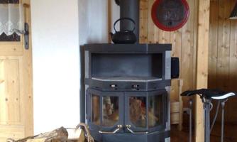 A cozy wood stove in a rustic room. Next to the stove is a basket of wood and some fireplace tools.