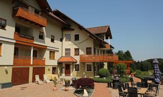 An inviting hotel building with a balcony and terrace. The outdoor area is equipped with chairs and tables as well as well-kept plants.