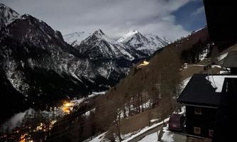 A stunning mountain landscape at night, with snow-capped peaks and twinkling lights in the valley. The sky is slightly cloudy, creating a calm atmosphere.