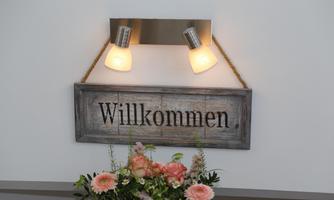 A wooden welcome sign with two lights above it. Below is a floral arrangement.