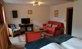 A cozy room with a red sofa, a TV, and a wooden chair. The decor is bright and inviting, with a rug and windows that let in daylight.
