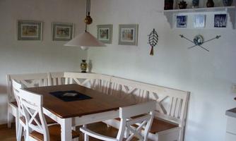 A cozy dining area with a large wooden table and white chairs. Artistic pictures and decorations hang on the wall.