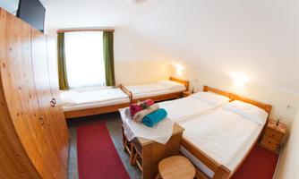 A cozy room with four beds and wooden furniture. The windows are adorned with green curtains and there are fresh towels on the beds.