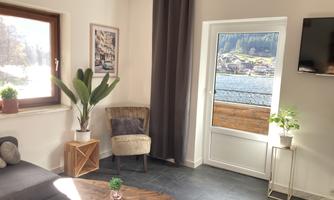 A cozy living room with a gray sofa, a wooden coffee table, and a window with a view. Plants and a warm light atmosphere create an inviting mood.