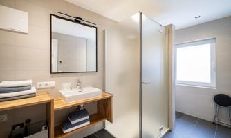 A modern bathroom with a walk-in shower and a sink on a wood shelf. Bright wall colors and a window provide cheerful light.