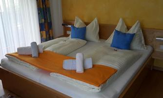 A cozy bedroom with a large double bed and colorful cushions. The room is bright and inviting, with plenty of natural light.