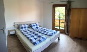 A cozy bedroom with two single beds and checkered bedspreads. Large windows provide plenty of daylight and a view of nature.