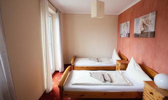 A cozy bedroom with two single beds and wooden furniture. The walls are beige and red, with artworks on the wall.