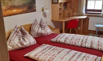 A cozy bedroom with a double bed and red-and-white bedding. There is a desk and a window overlooking the outdoors.