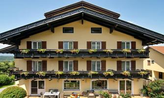 A charming building in rural style with several balcony flowers. The facade is yellow, and the windows have brown shutters.