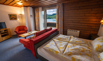 A cozy hotel room with a double bed and a red sofa. Large windows offer a view of the landscape.