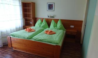 A cozy bedroom with two single beds and green bed linen. There is a wooden wardrobe and plenty of daylight through the window.