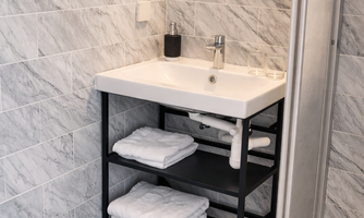 A modern bathroom with gray tiles and a vanity. Towels are on a black shelf under the sink.