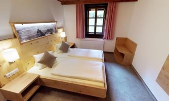 A bright bedroom with two single beds and a wooden design. Large windows provide plenty of daylight and a cozy atmosphere.