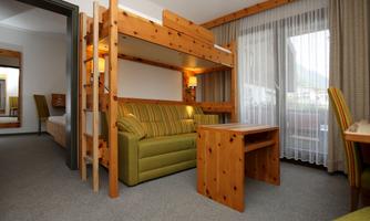 A cozy room with a wooden loft bed and a green couch. There is a small table and plenty of daylight coming through the window.