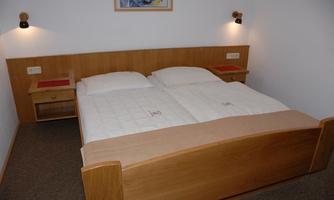 A simple bedroom with a double bed and nightstands. The walls are light, and the lighting is soft.